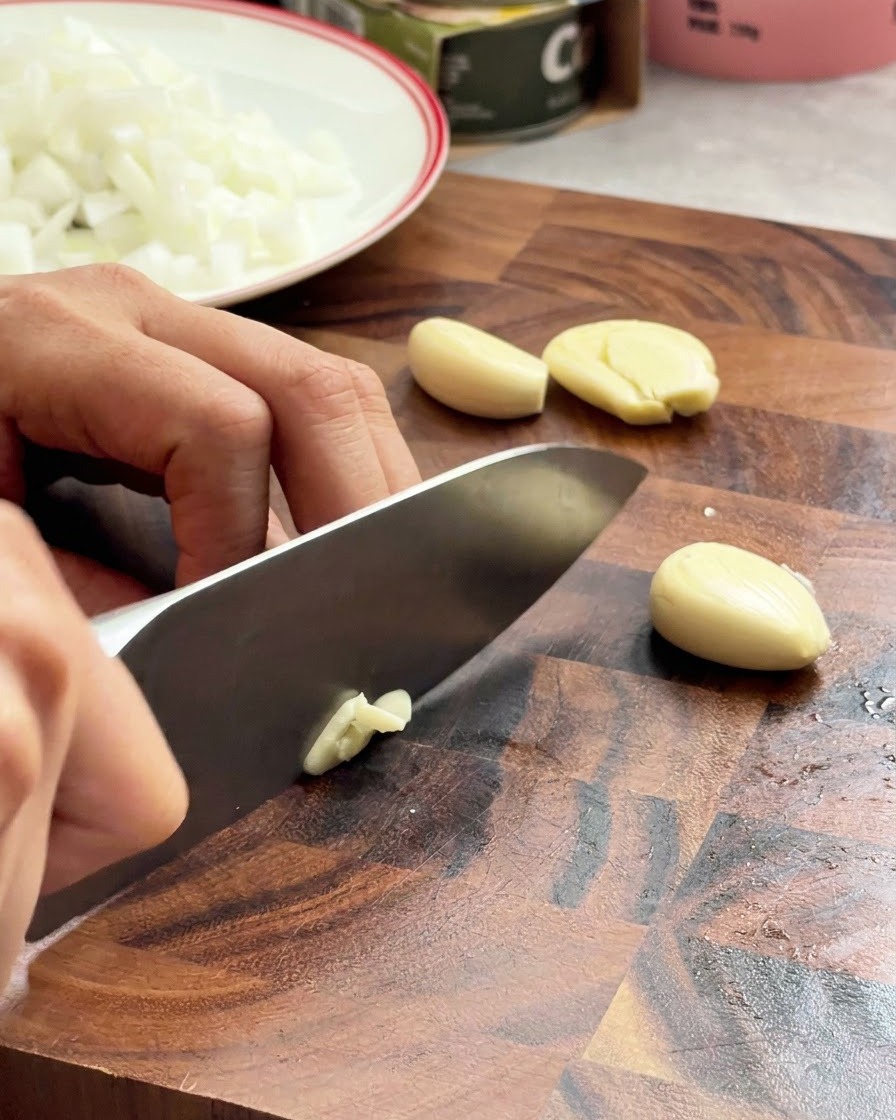 Dientes de ajo siendo picados finamente con un cuchillo de chef sobre una superficie de madera.