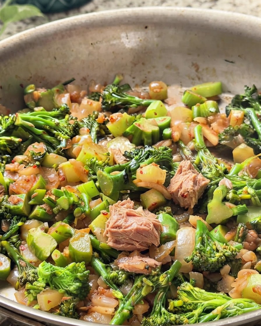 Trozo de atún en lata mezclado dentro de la sartén con brócoli verde y cebollas.
