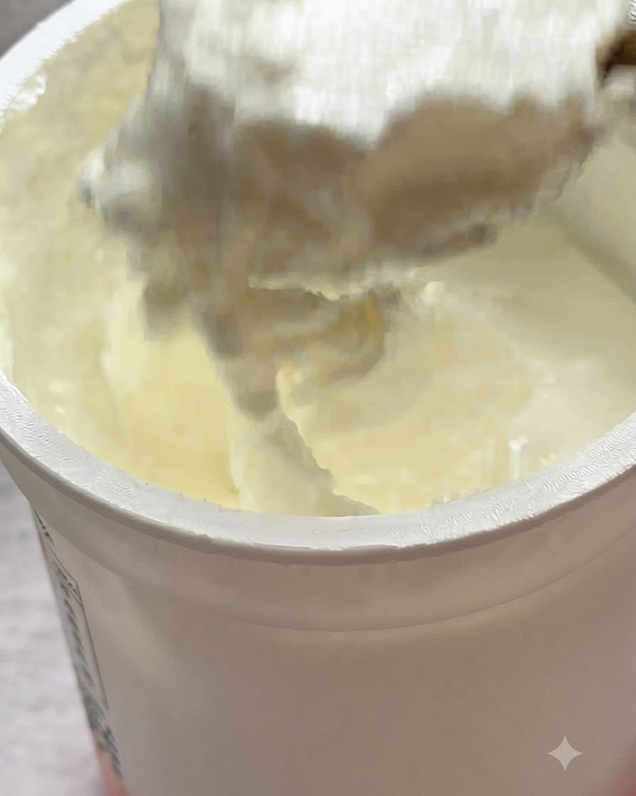 Una cucharada de yogur natural siendo añadida encima de la pasta en una sartén.