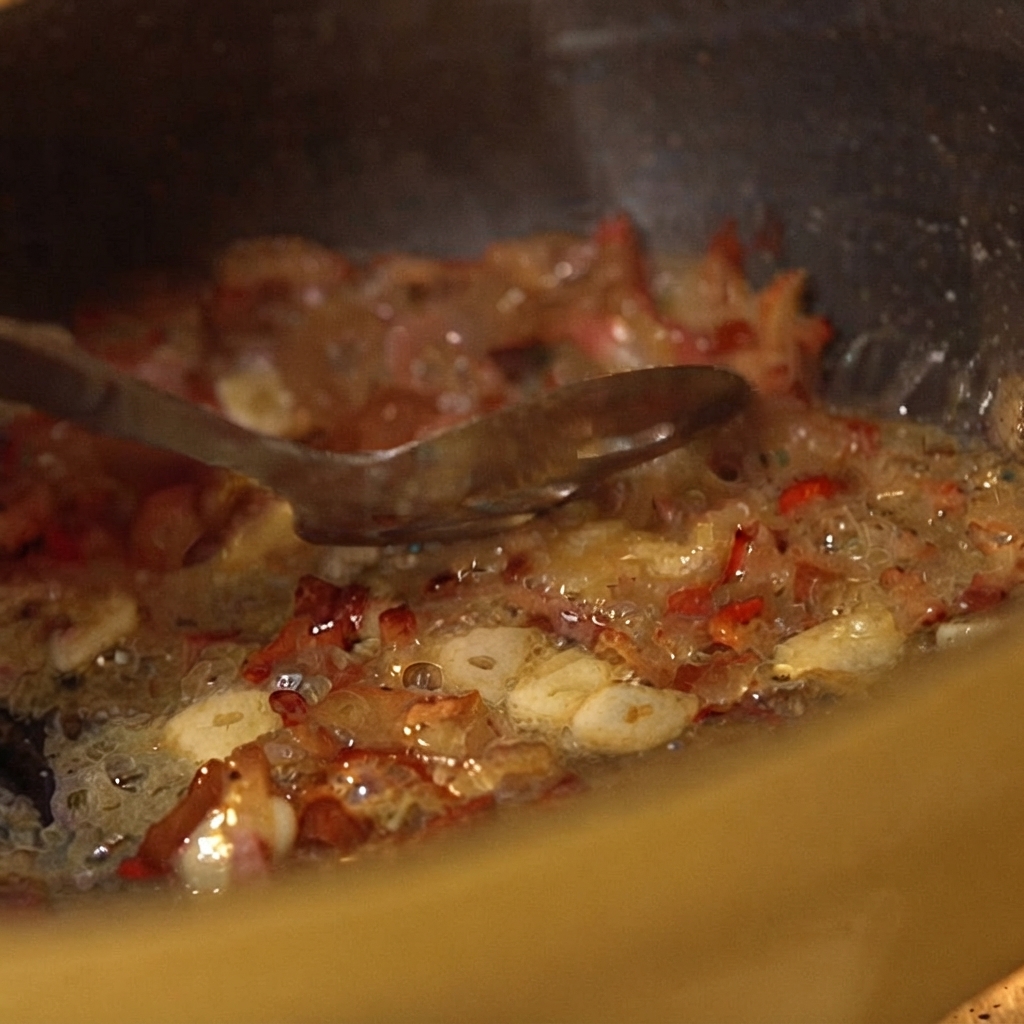 Tomates triturados enlatados siendo mezclados con los ingredientes de la sartén chisporroteante usando una cuchara.