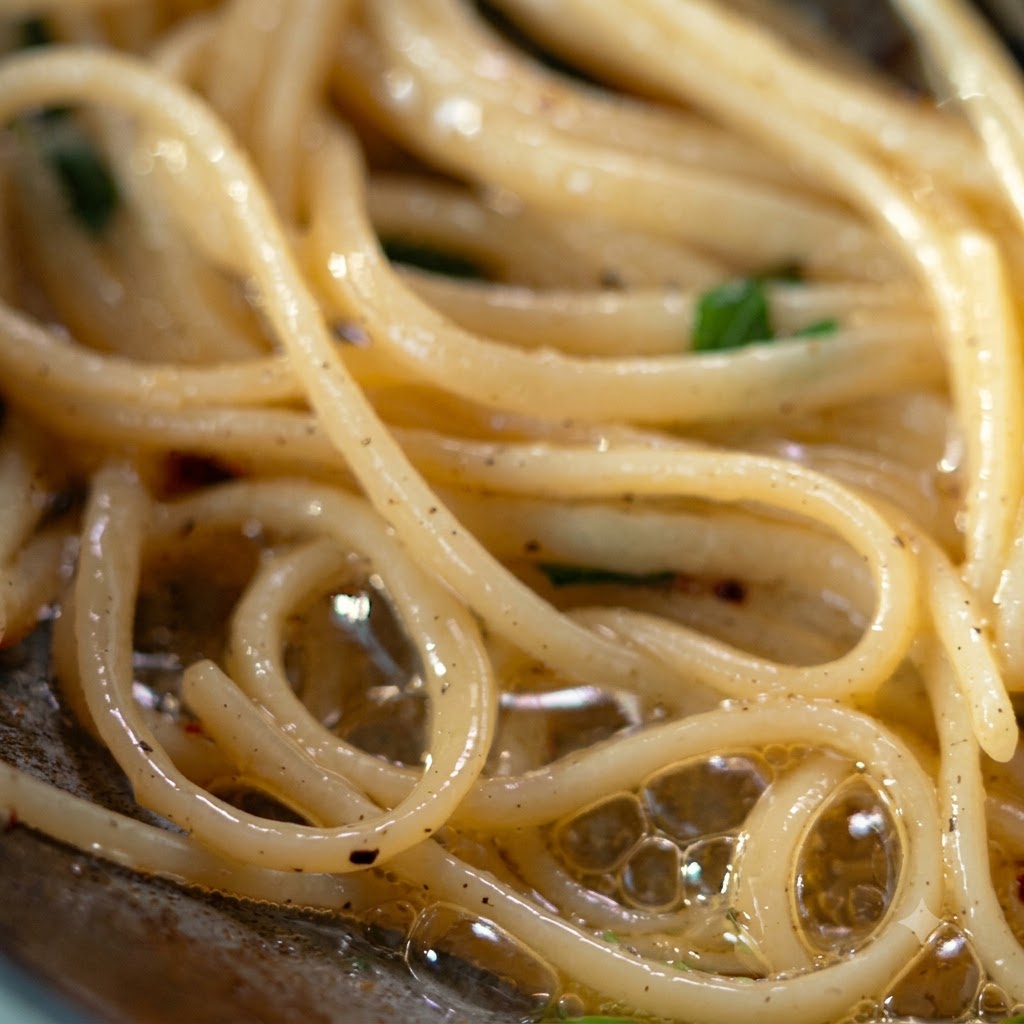 Un cucharón y pinzas levantando y transfiriendo pasta sazonada hacia un plato plateado.