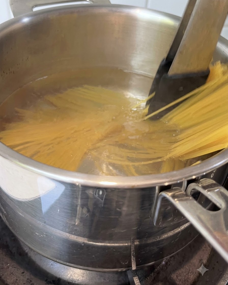 Espaguetis siendo revueltos con pinzas en una olla con agua hirviendo.