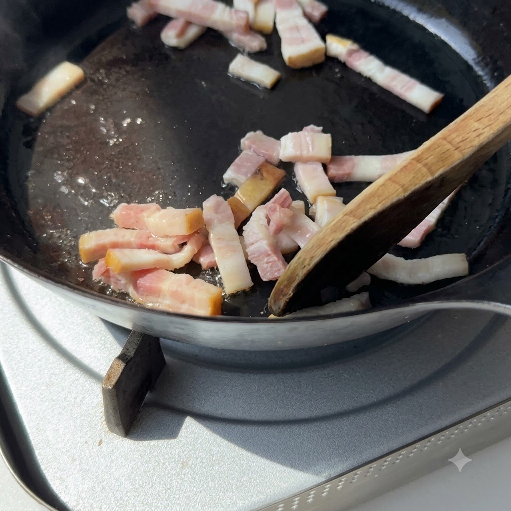 Una espátula de madera removiendo trozos de tocino en una sartén de hierro fundido sobre la estufa.