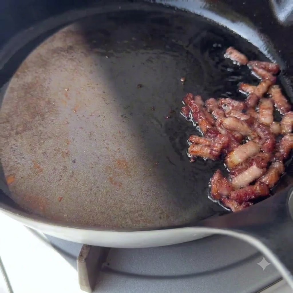 Trozos de tocino dorados chisporroteando en un lado de una sartén caliente.