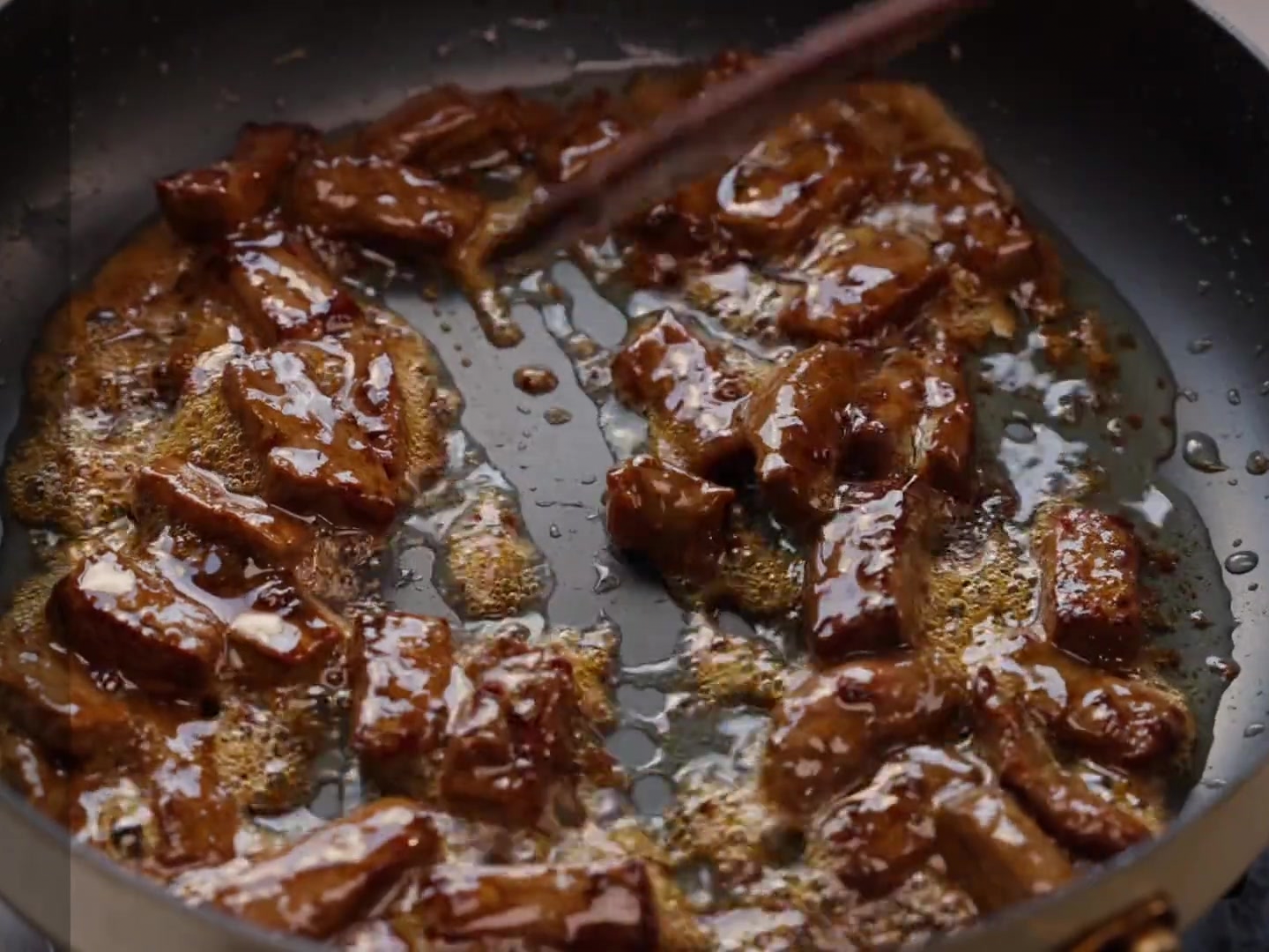 Pimientos cortados en rodajas y cebollas siendo mezclados en una sartén con trozos de bistec marrón.
