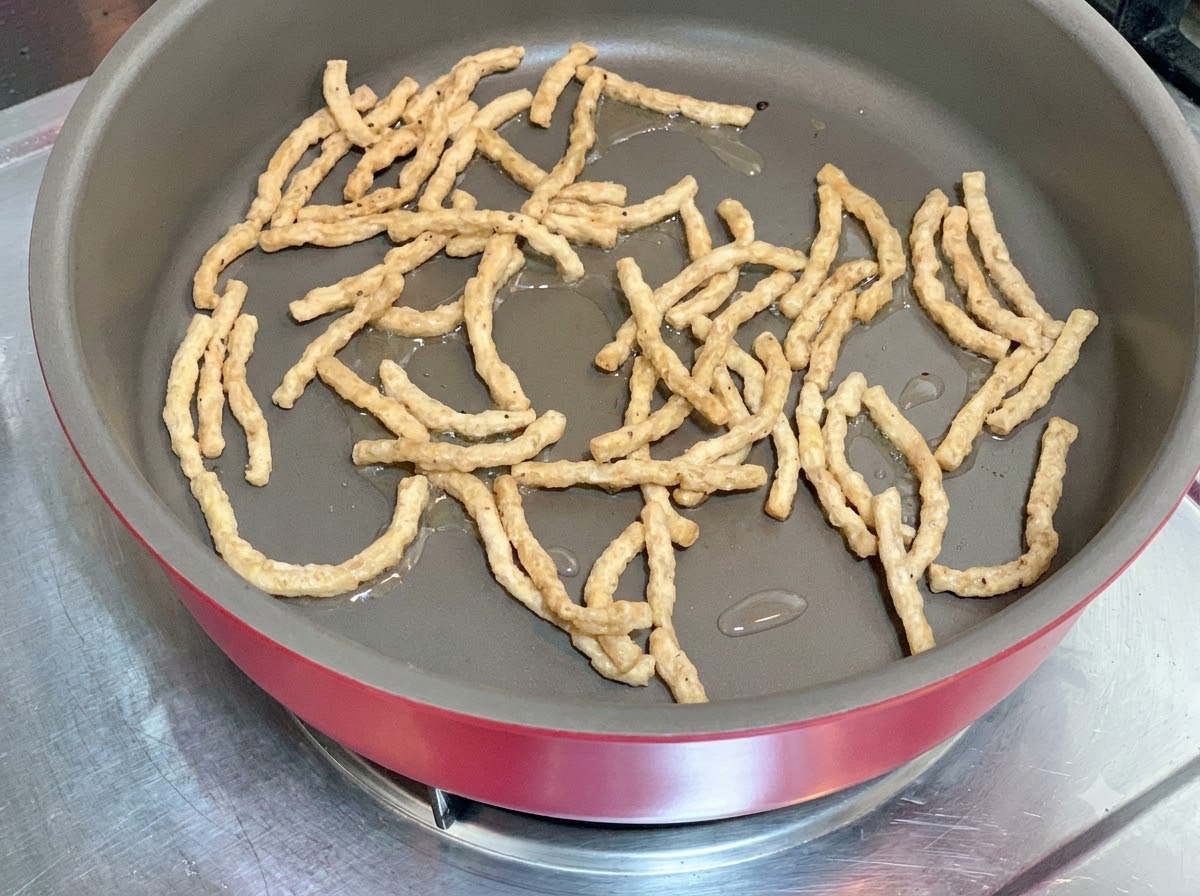 Tiras de proteína vegetal siendo salteadas en una sartén caliente con una pequeña cantidad de aceite.