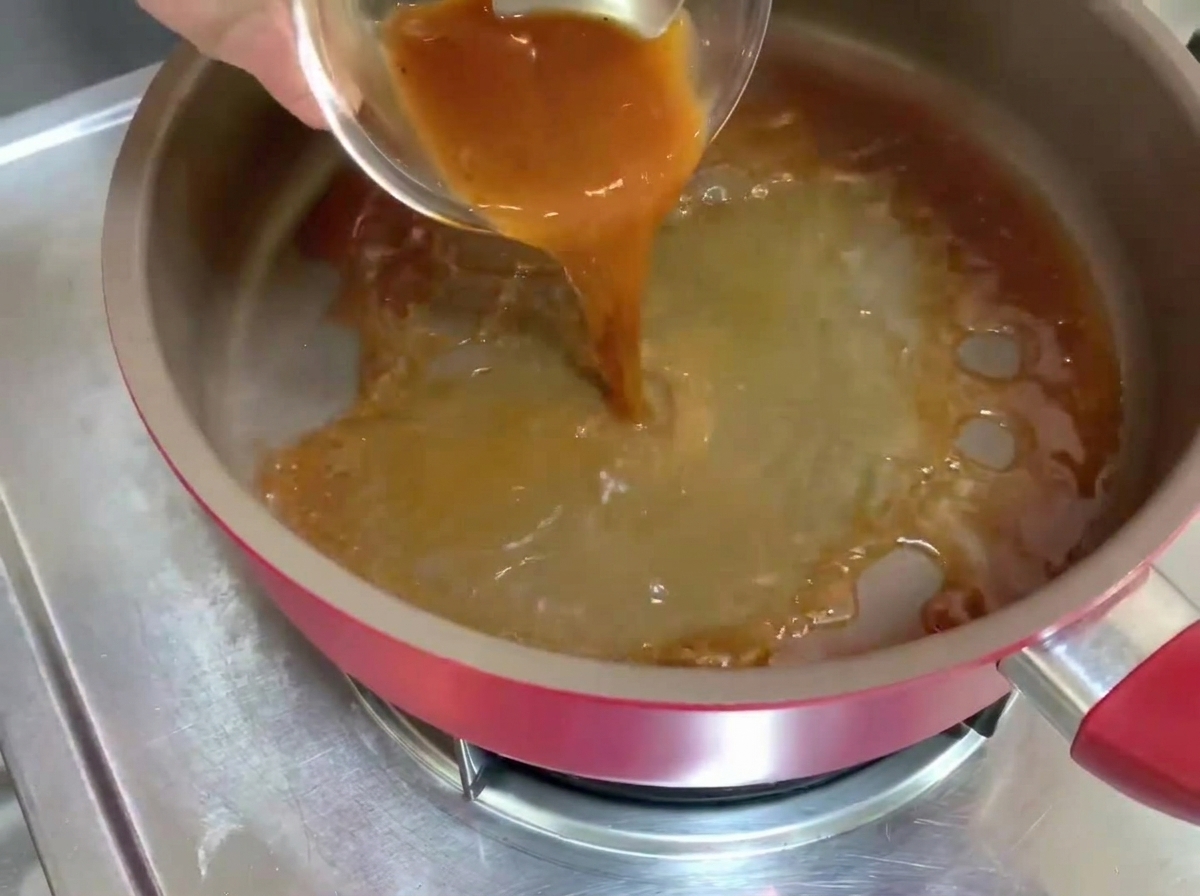 Salsa de pimienta negra siendo vertida en una sartén caliente, creando líquido burbujeante.