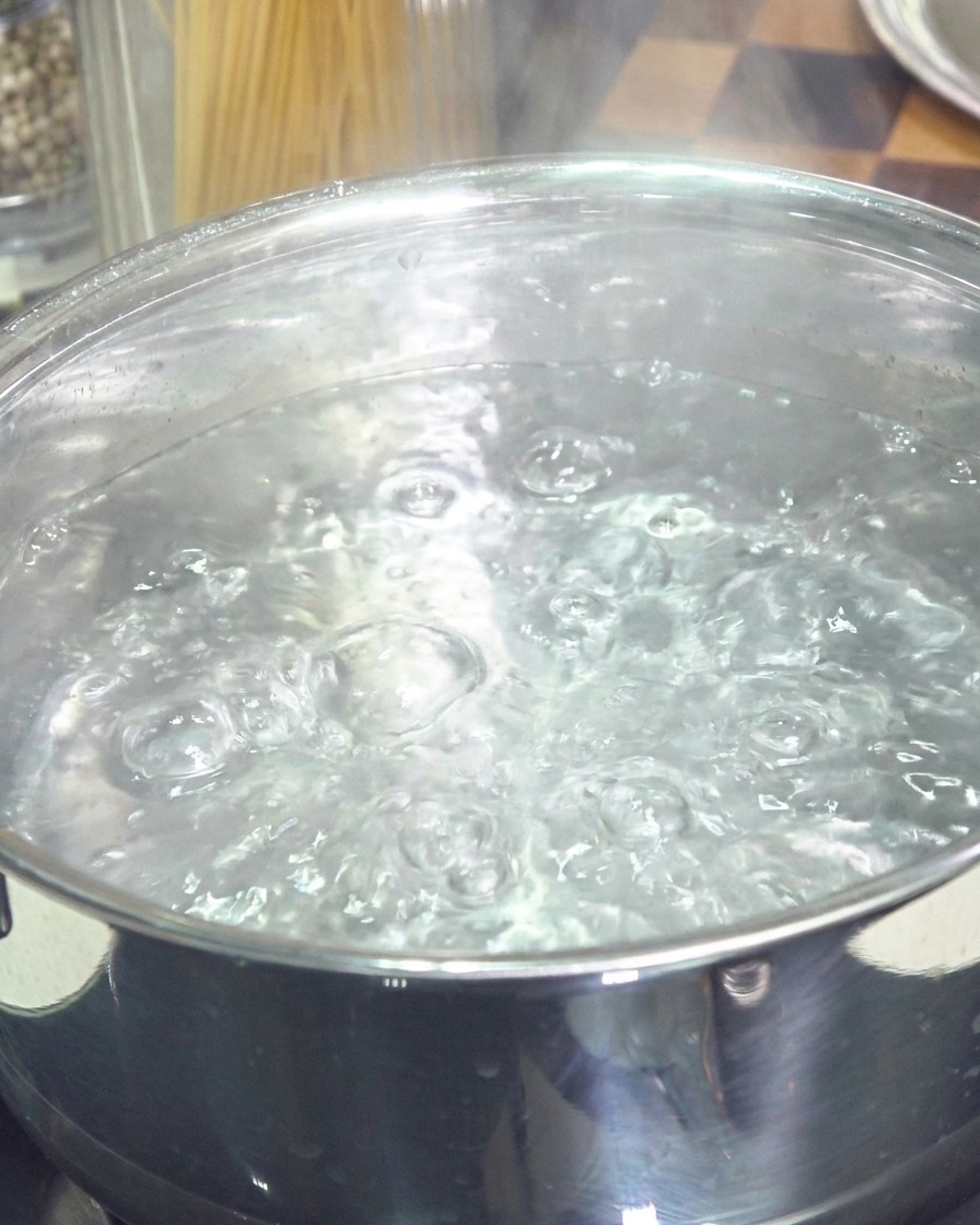 Una olla de acero inoxidable llena de agua hirviendo a borbotones con burbujas que ascienden a la superficie.