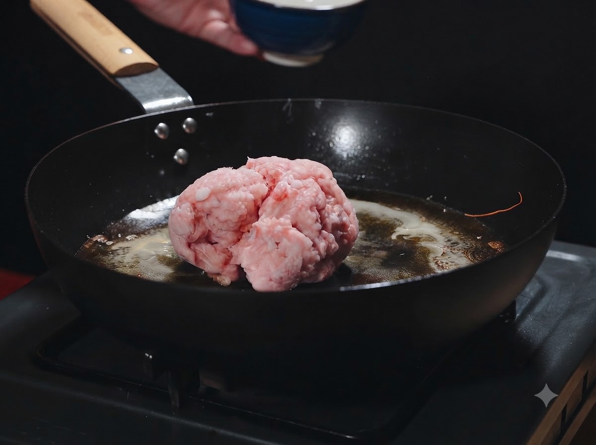 Una bola de carne picada cruda reposando en una sartén caliente con aceite de camarón mientras se añade.