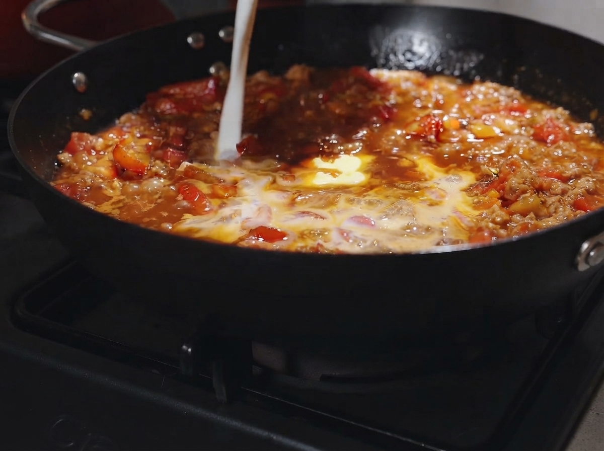 Un trozo de mantequilla y un chorrito de leche vertiéndose en la salsa burbujeante de tomate y carne.