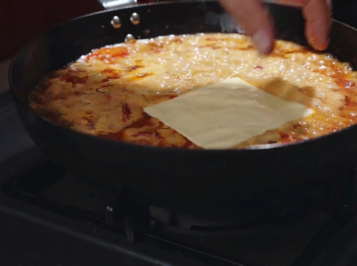 Una rodaja de queso colocada plana sobre la salsa cremosa burbujeante en la sartén.