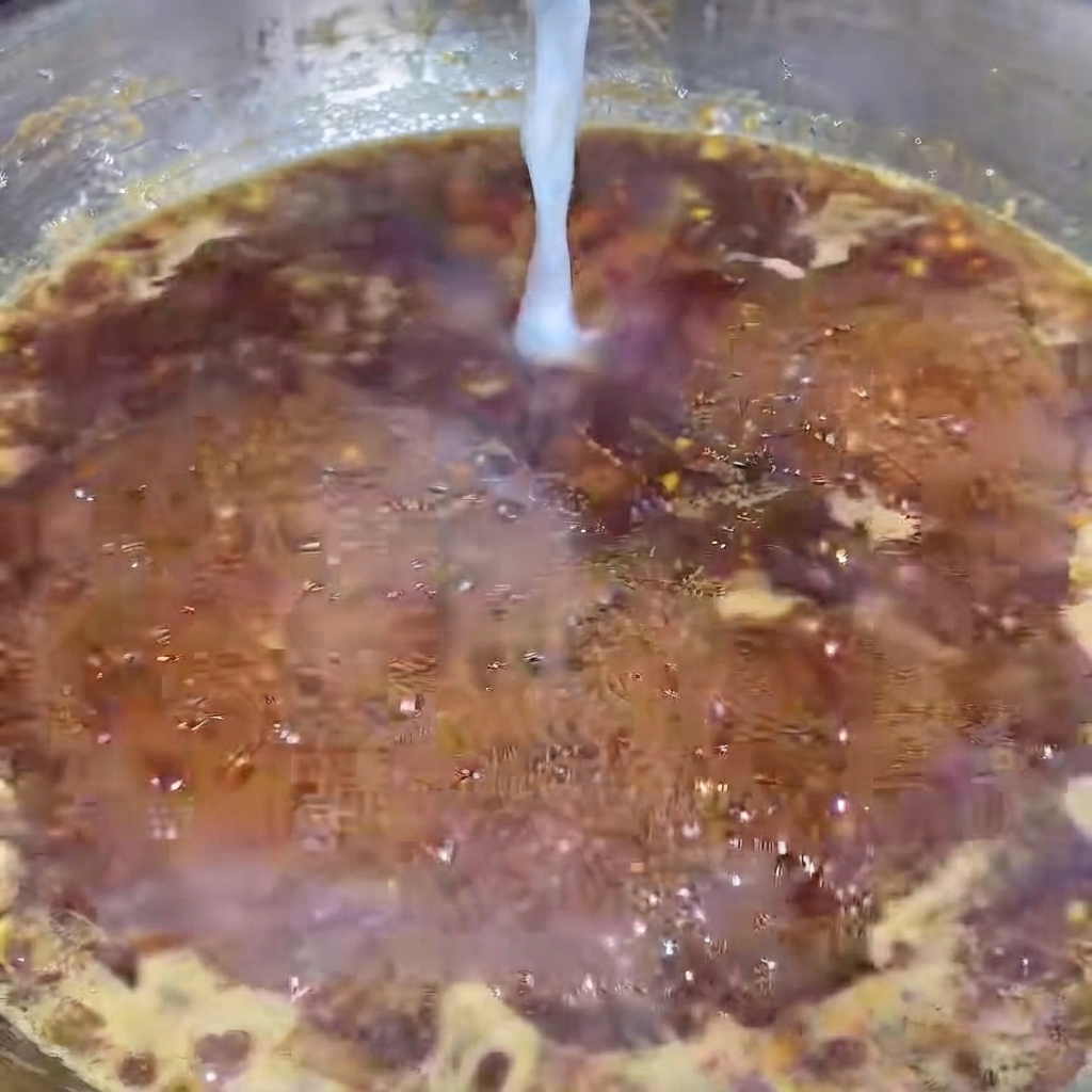 Un hilo fino de agua con almidón blanco siendo vertido en una salsa de pimienta negra oscura y burbujeante en una sartén caliente.