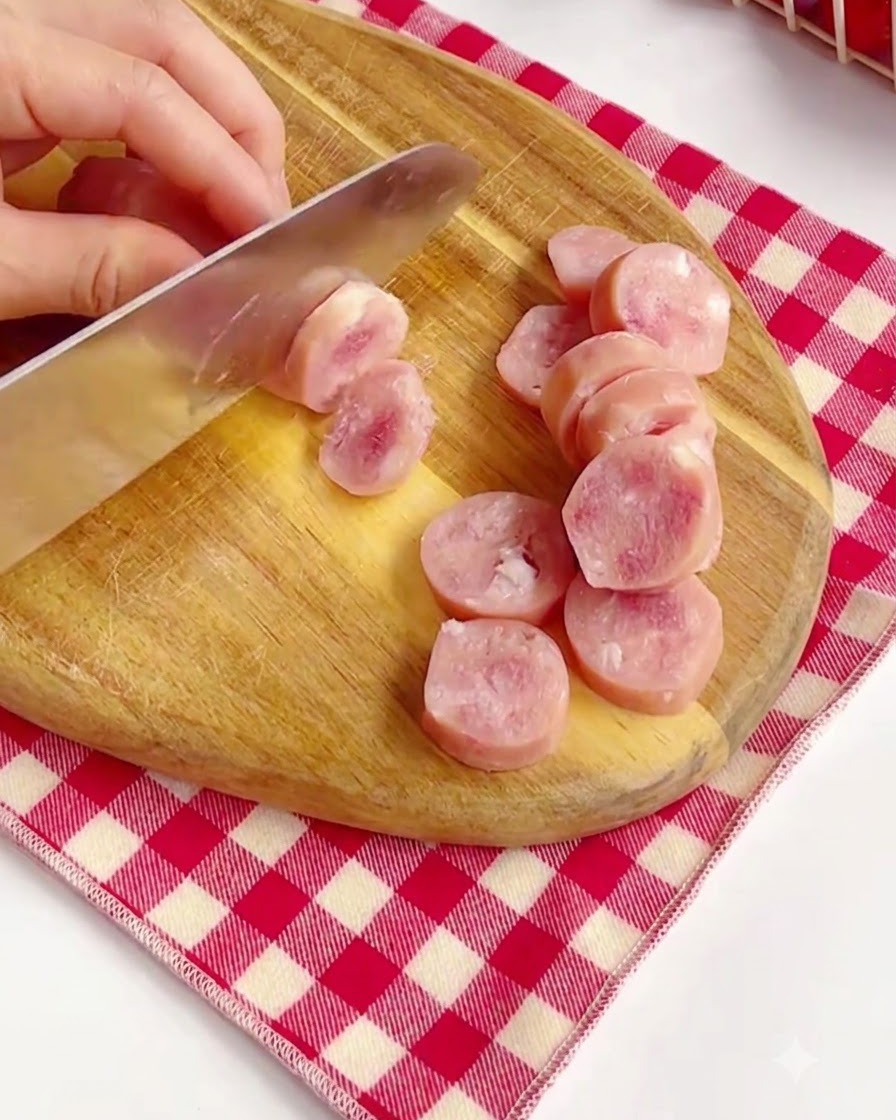 Cortando salchichas rosadas en rodajas sobre una tabla de cortar de madera.