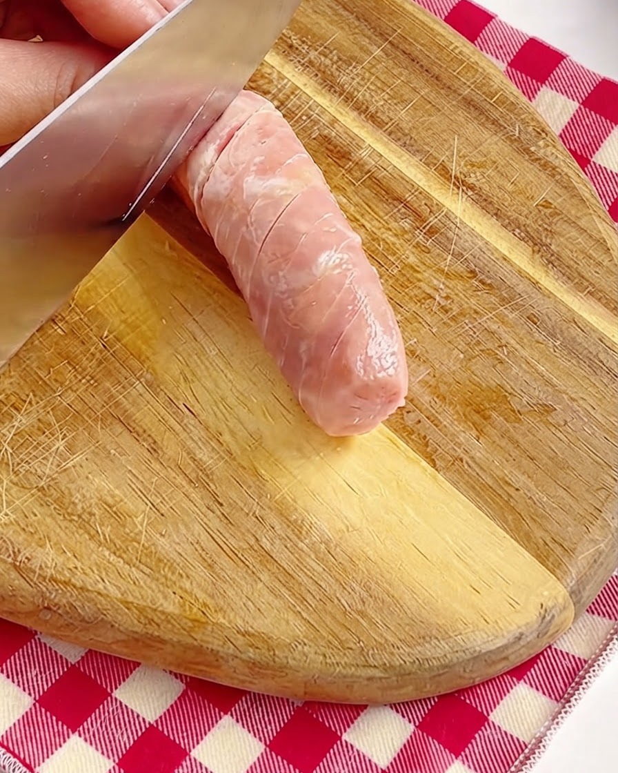 Una mano marcando cuidadosamente la superficie de una salchicha entera con un cuchillo en una tabla de madera.