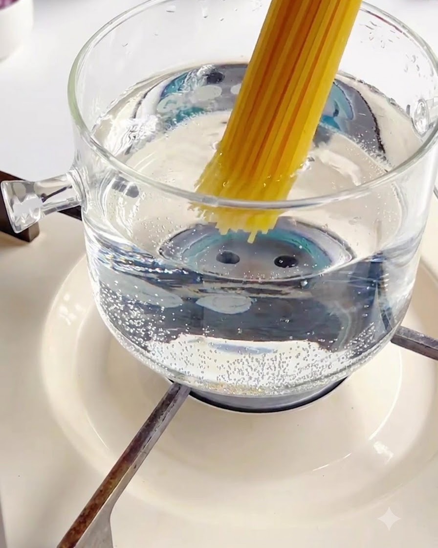 Introduciendo un paquete de fideos de espagueti secos en una olla de vidrio burbujeante con agua caliente.