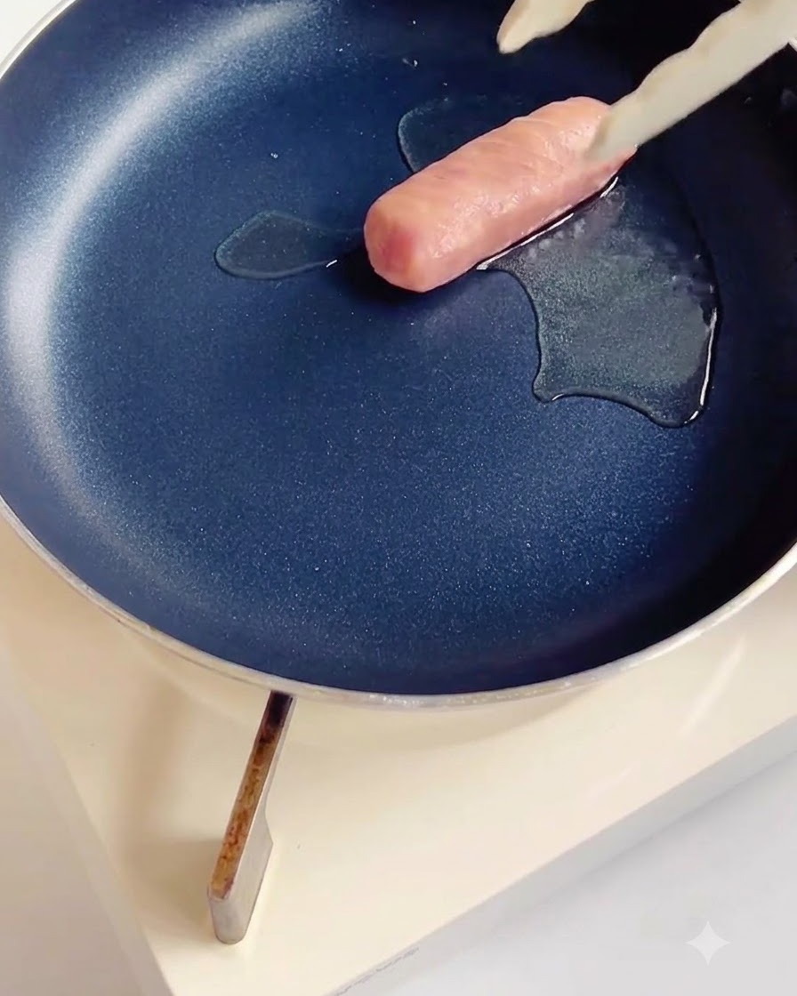 Salchicha marcada friéndose en una sartén antiadherente oscura con una pequeña cantidad de aceite.