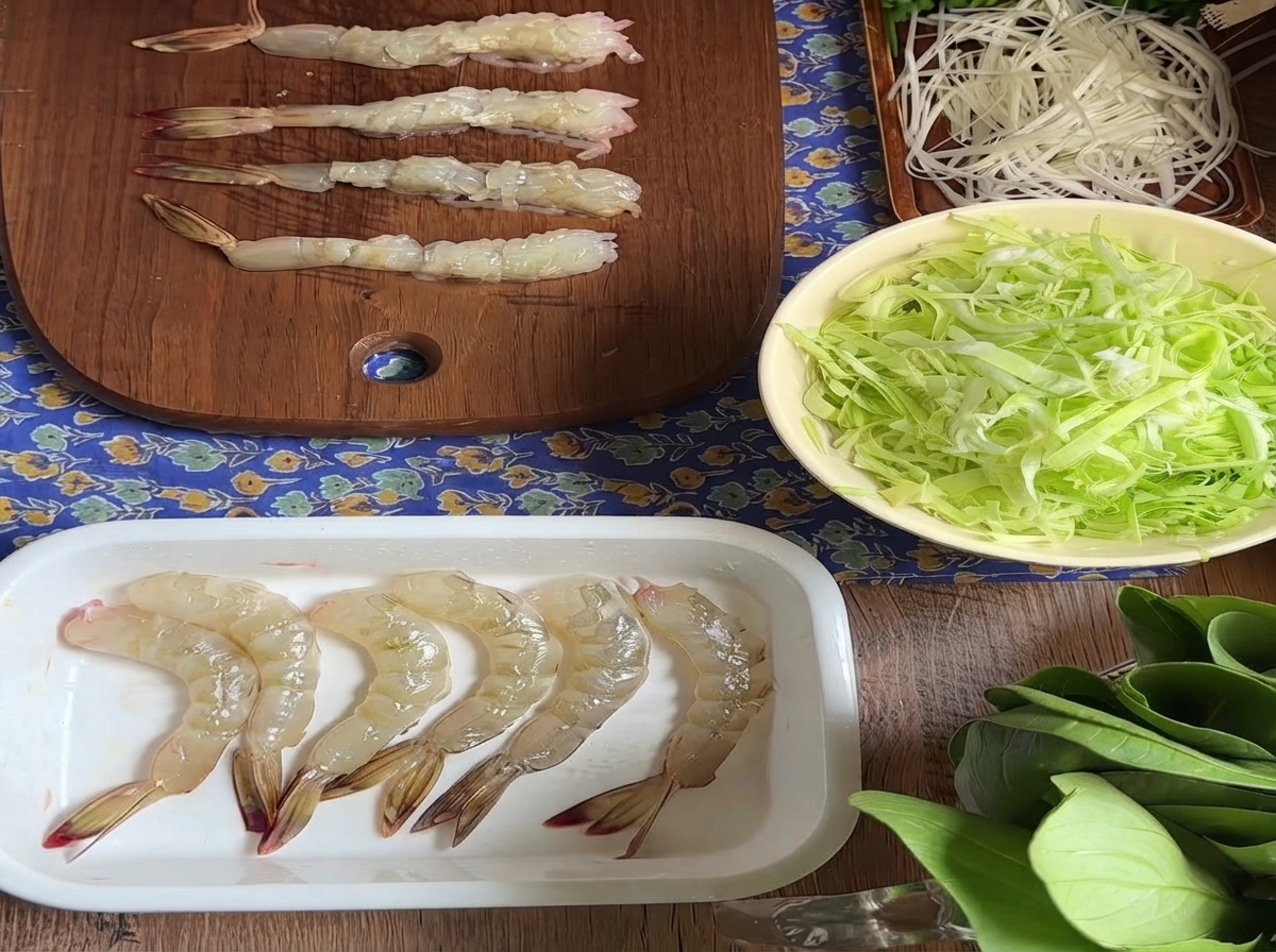 Varios camarones crudos pelados alineados en una tabla de cortar de madera tras preparar los tendones del vientre.