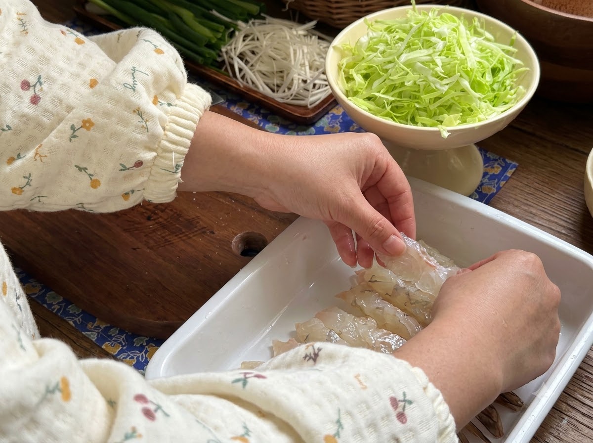 Manos presionando camarones crudos en una bandeja blanca para prepararlos para el marinado.