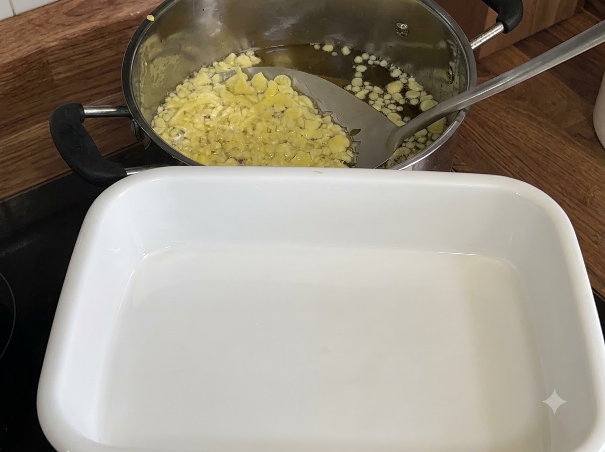 Una espumadera sacando copos de tempura fritos de color amarillo pálido de una olla con aceite caliente hacia una bandeja blanca.