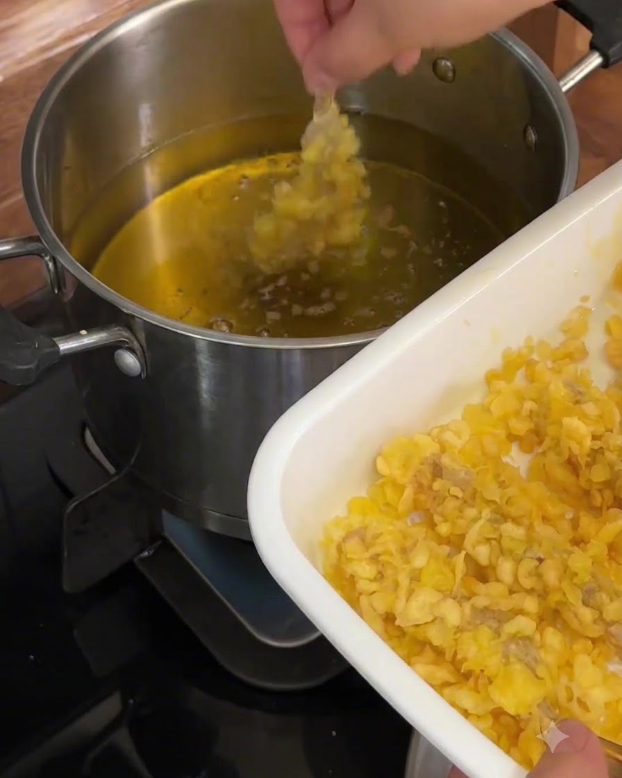 Un camarón rebozado siendo sumergido en aceite caliente dentro de una olla de metal.