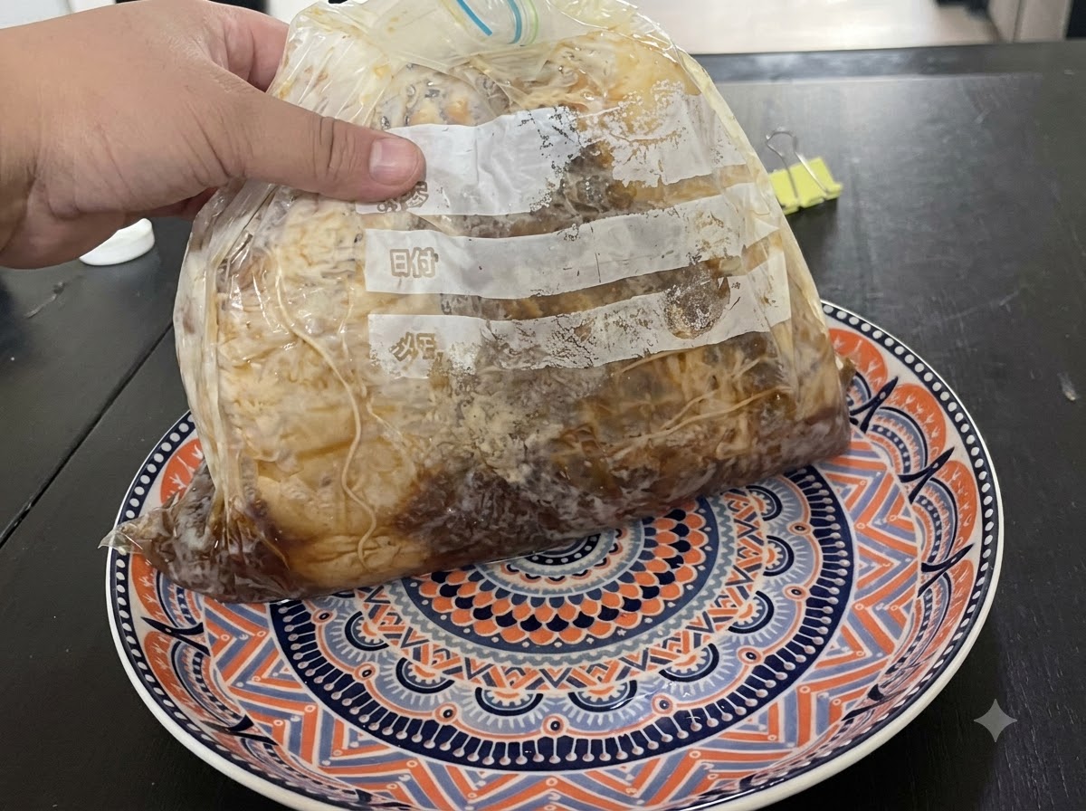 Una mano sosteniendo una bolsa sellada al vacío con carne marinada sobre un plato decorado.