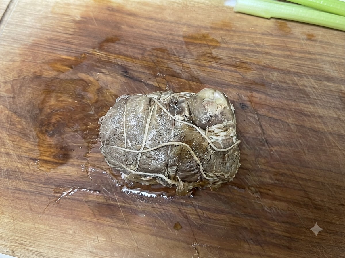 Rollo de cerdo chashu atado descansando sobre una tabla de cortar de madera antes de ser cortado.
