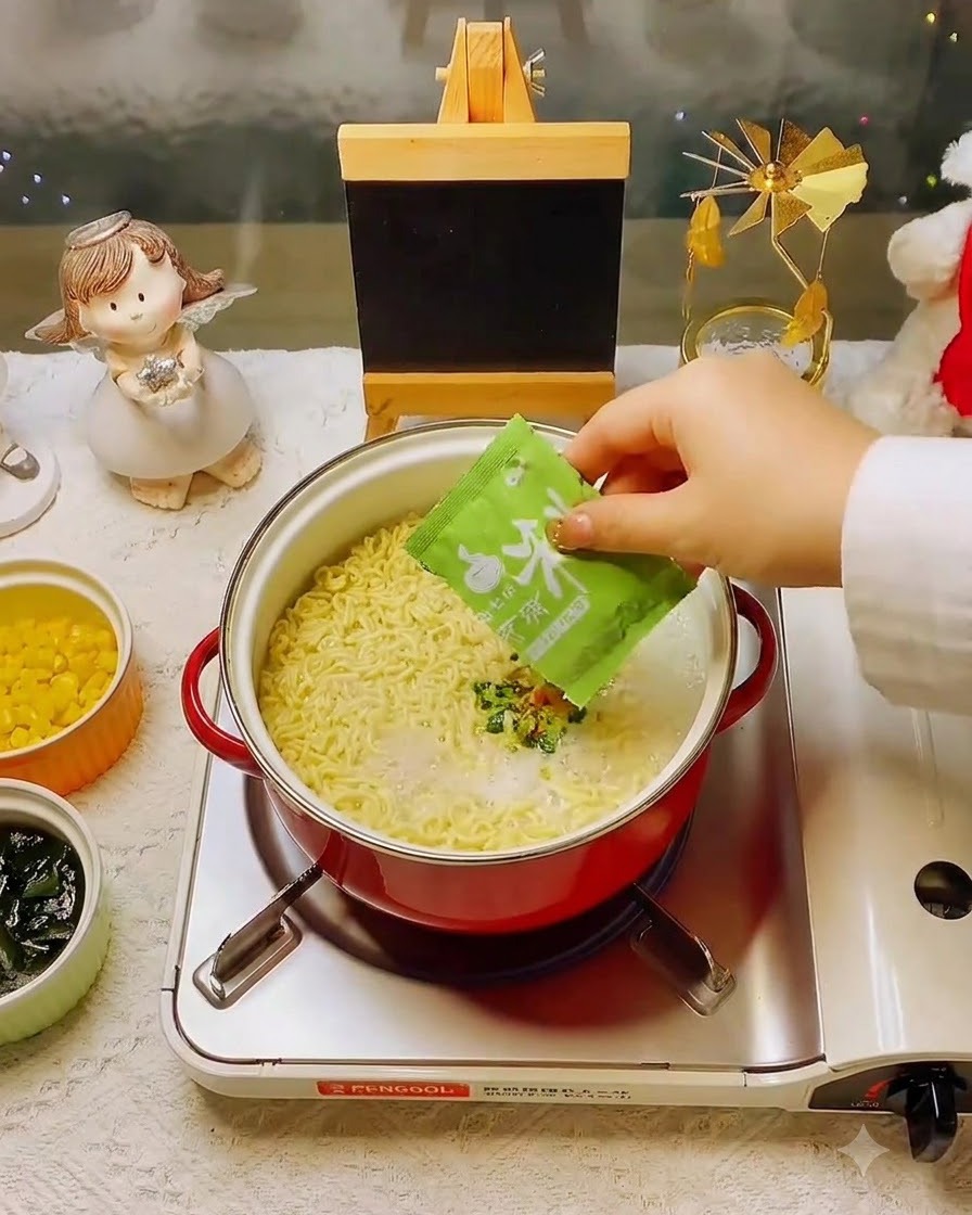 Una mano añadiendo un paquete de condimento verde en la olla de fideos y caldo.