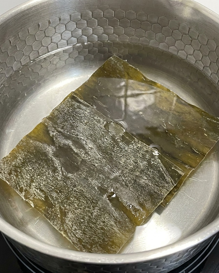 Trozos de alga kelp deshidratada en remojo en una olla con agua a fuego lento.