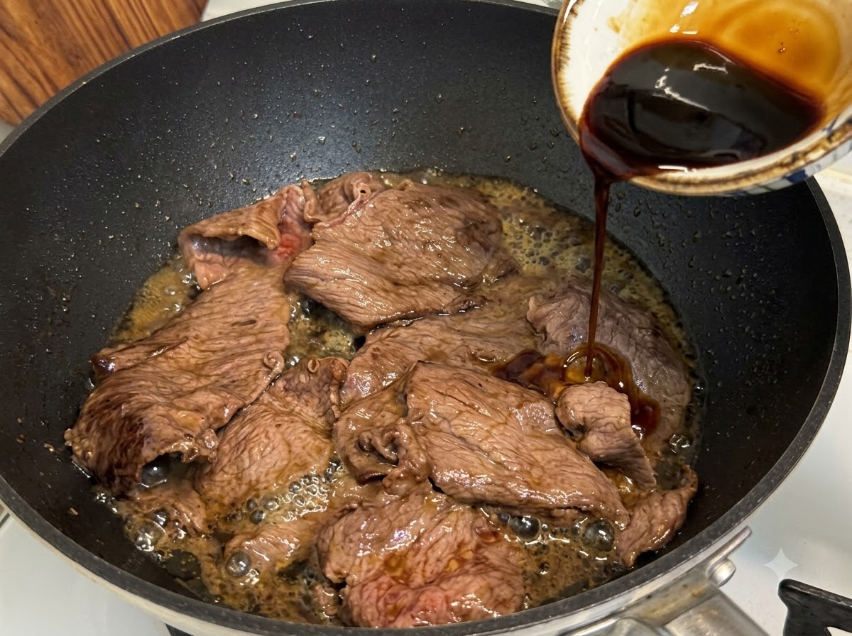 Salsa teriyaki vertiéndose en una sartén sobre carne de res grasa en rodajas para cocinar a fuego lento y reducir.