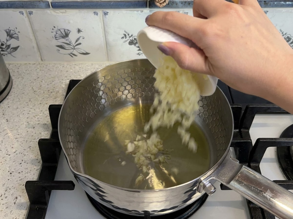 Ajo picado y tomates en dados añadiéndose a aceite caliente en una olla para sofreír.