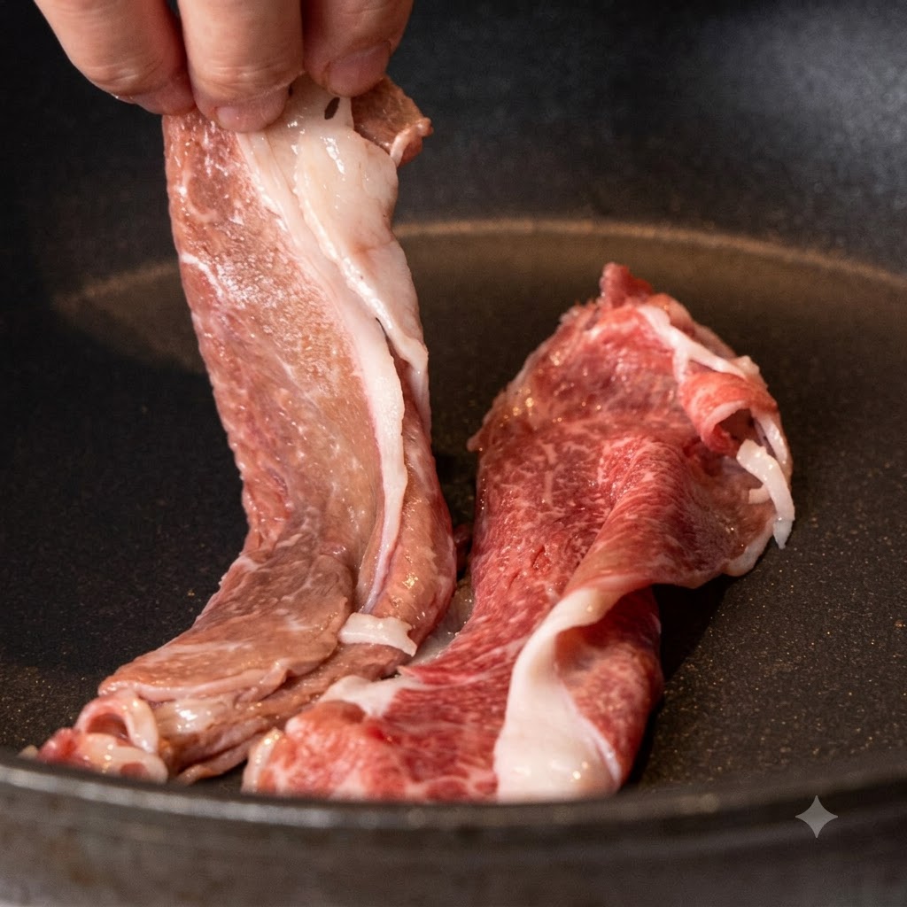 Tiras de aguja de ternera wagyu siendo colocadas en una sartén antiadherente seca y caliente.