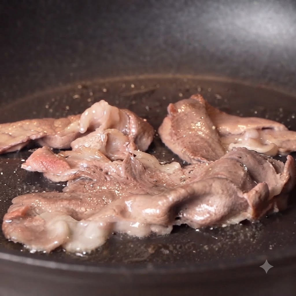 Pimienta negra y sal siendo espolvoreadas sobre tiras de ternera sellada cocinándose en una sartén.