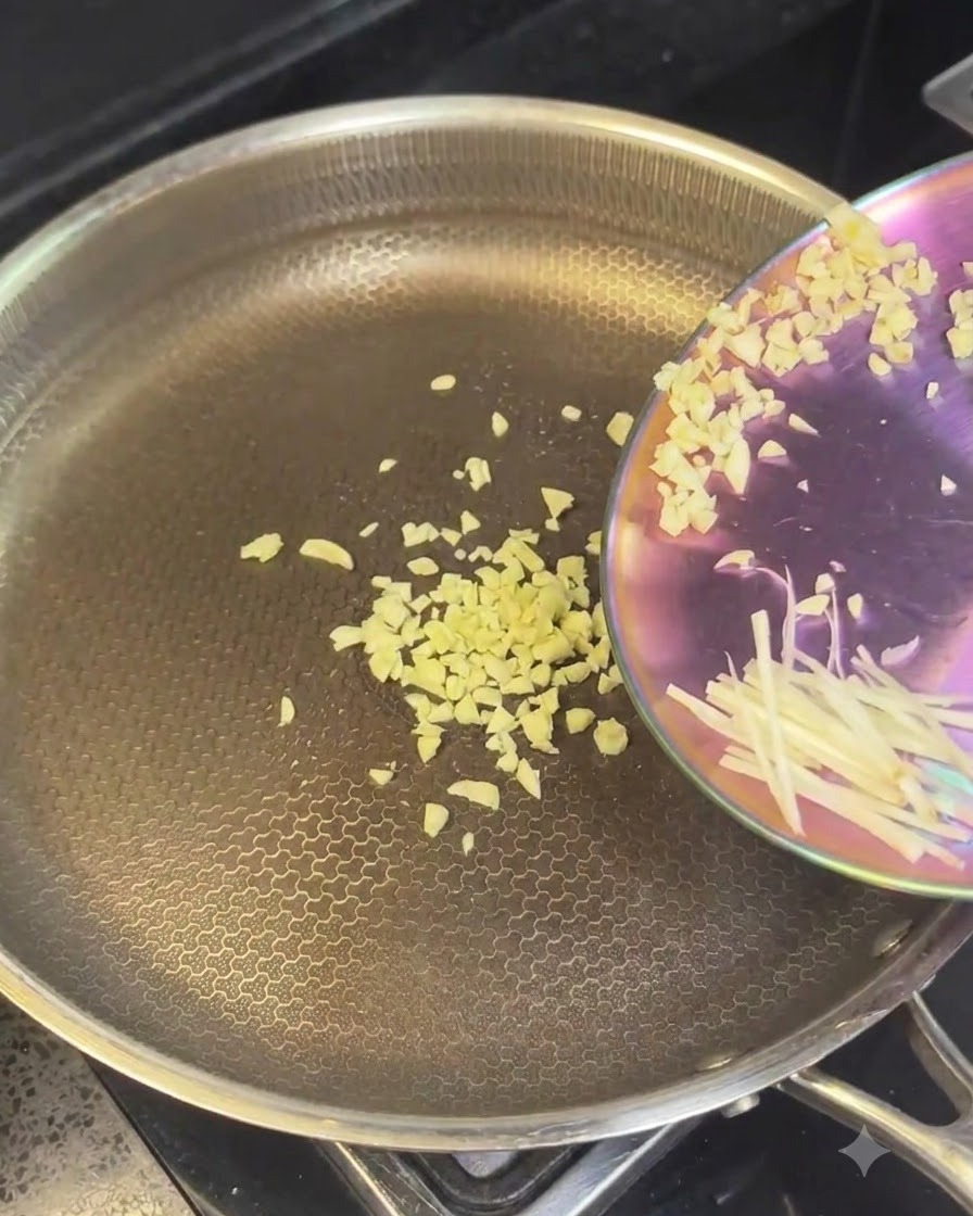Ajo picado y cebolla cortada vertiéndose en una sartén caliente de acero inoxidable.