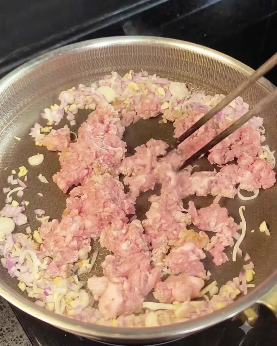 Carne picada cruda colocada en el centro de una sartén rodeada de cebolla y ajo sofritos.