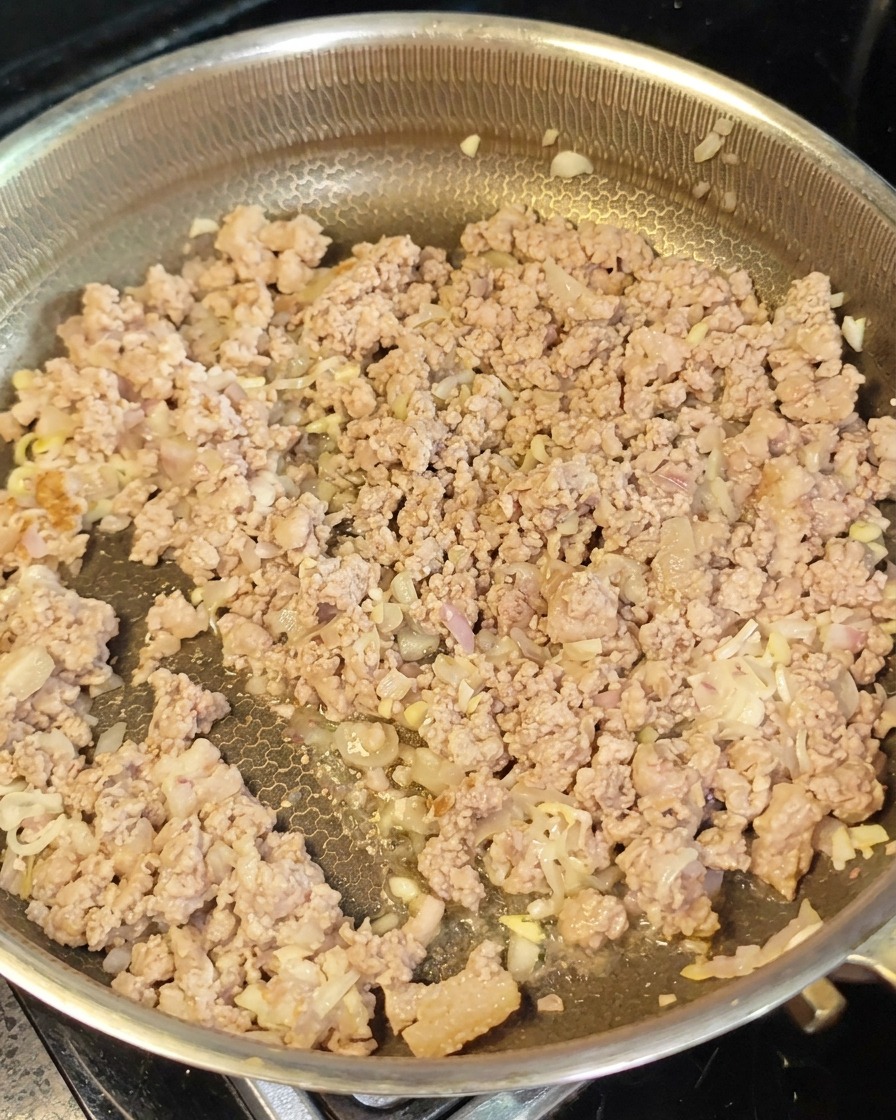 Carne picada dorada y aromáticos extendidos en una sartén incorporando pasta de miso rojo.