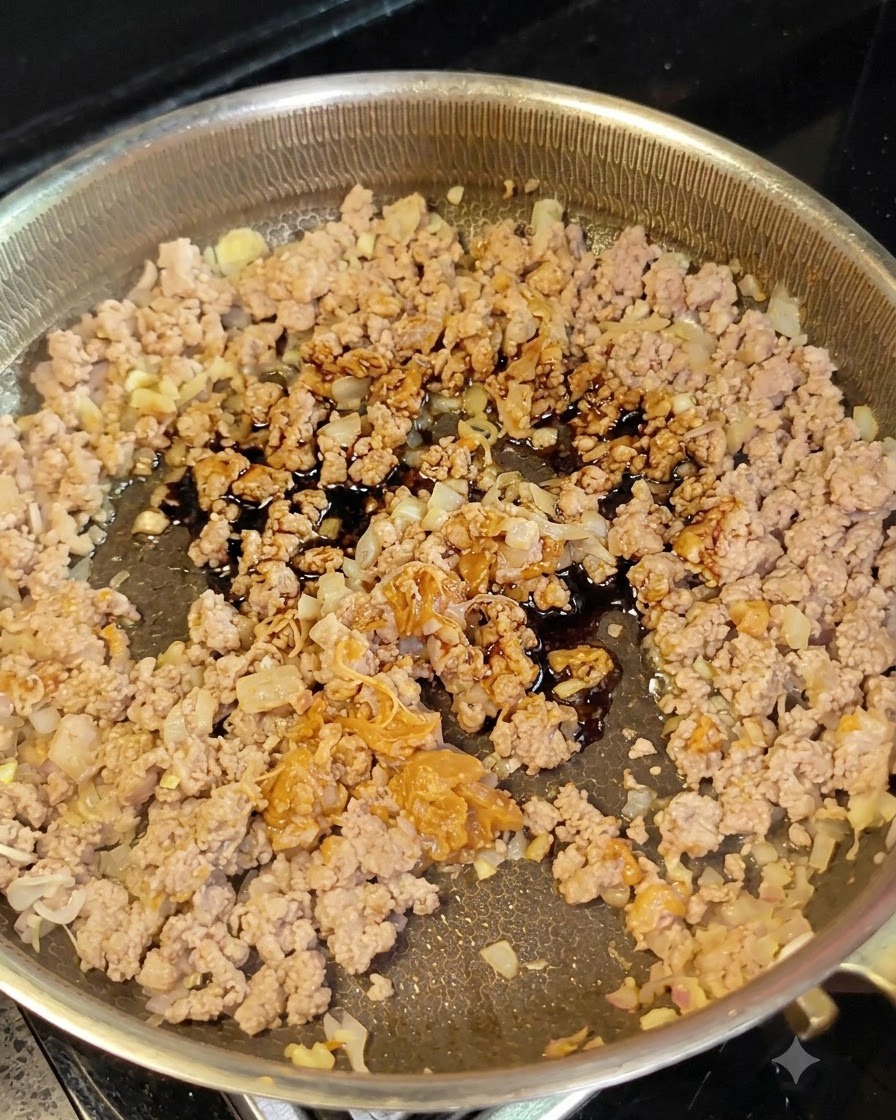 Salsa de soja oscura cayendo desde una pequeña cuchara sobre la carne picada y las cebollas en una sartén.
