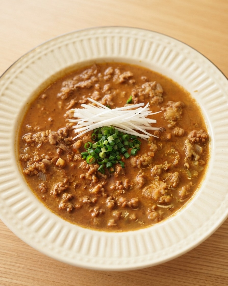 Tiras finas de cebollino blanco y cebolletas picadas dispuestas ordenadamente sobre una rica salsa de carne en un bol de servicio blanco.