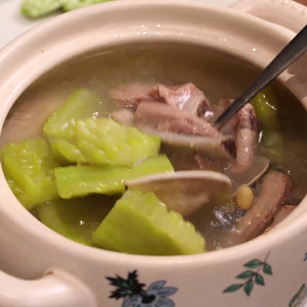 Una cuchara de metal saca costillas de cerdo cocidas, almejas y melón amargo de una olla de sopa.