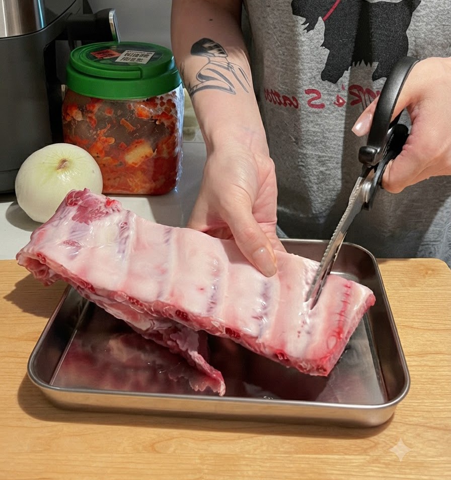 Manos usando tijeras de cocina para cortar un costillar grande de costillas de cerdo crudas en piezas individuales sobre una tabla de cortar de madera.
