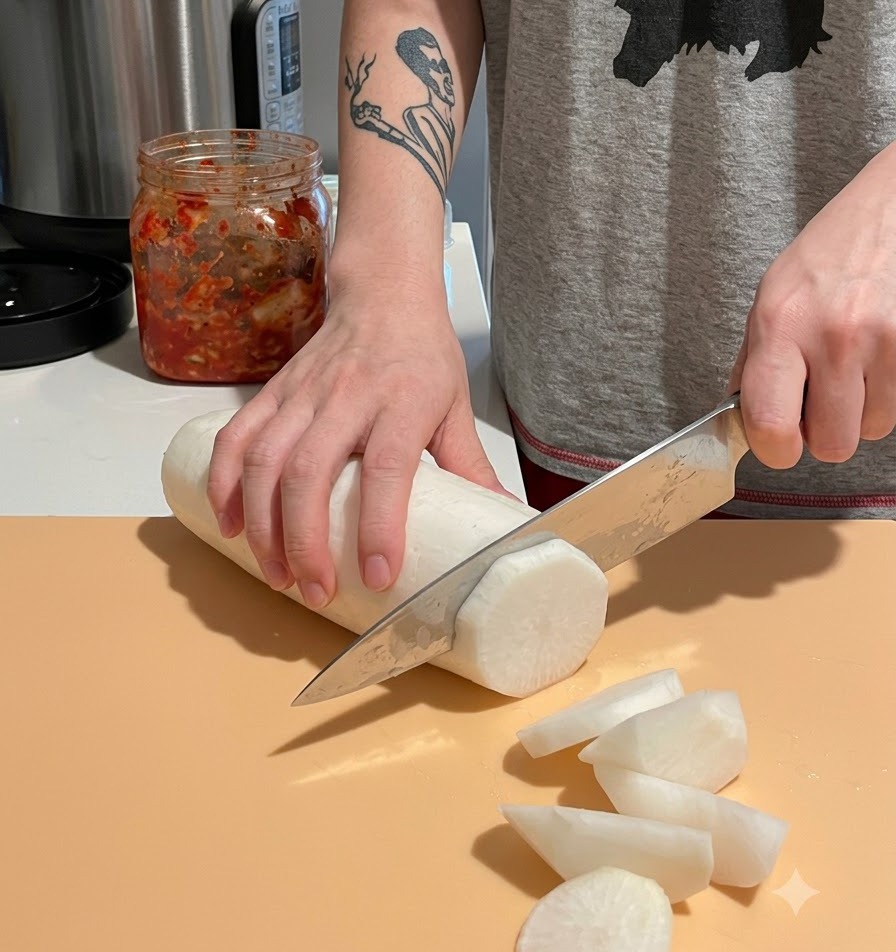 Cortando un rábano daikon blanco pelado en trozos grandes y gruesos sobre una tabla de cortar.