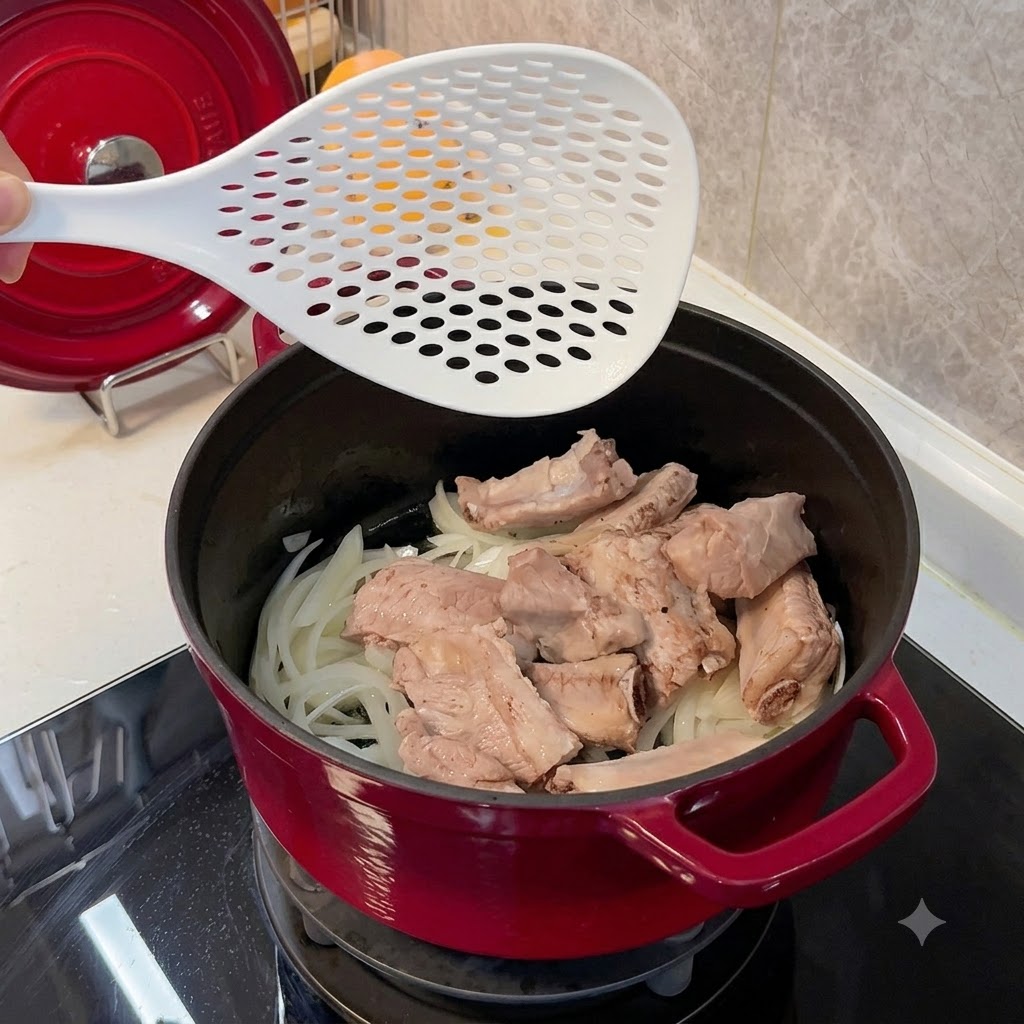 Colocando costillas de cerdo blanqueadas en una olla roja sobre una cama de cebollas ablandadas usando una espumadera blanca.