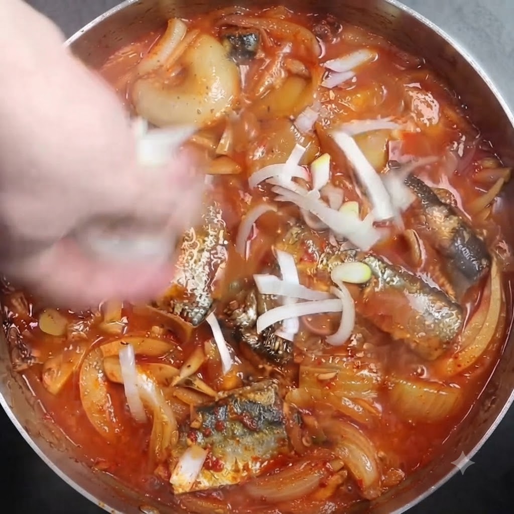 Cebollines blancos picados siendo espolvoreados sobre una olla humeante de pescado estofado.