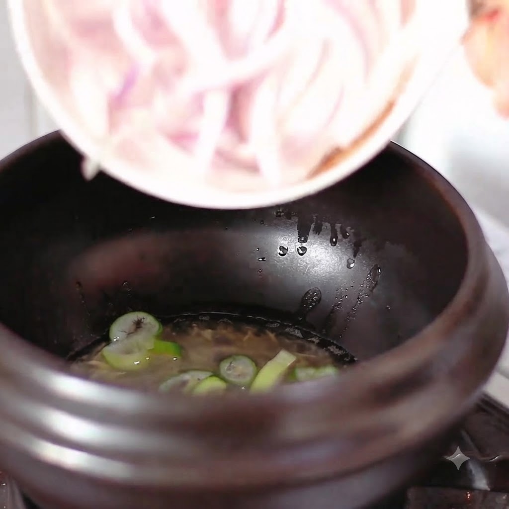 Rodajas de cebolla roja cayendo desde un cuenco blanco hacia una olla con aceite y cebolleta picada.