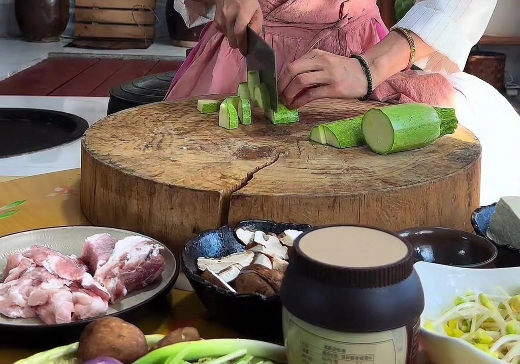 Manos picando un calabacín verde en piezas triangulares con un cuchillo en una tabla de cortar redonda de madera.