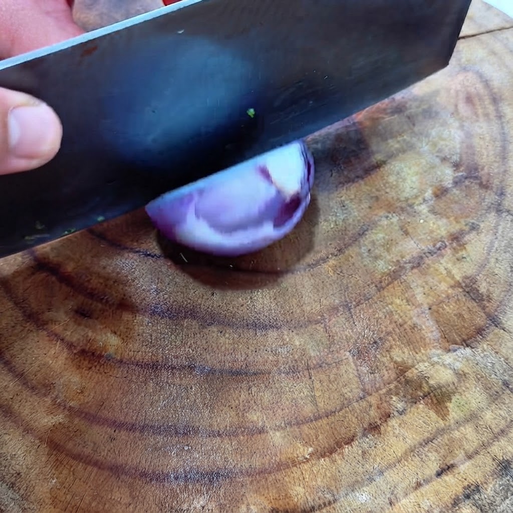 Un gran cuchillo de chef picando media cebolla roja en una superficie de madera.