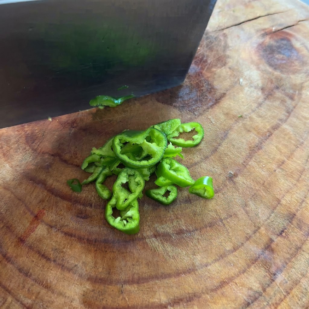 Chiles verdes siendo cortados en aros finos con un cuchillo sobre una tabla de cortar.