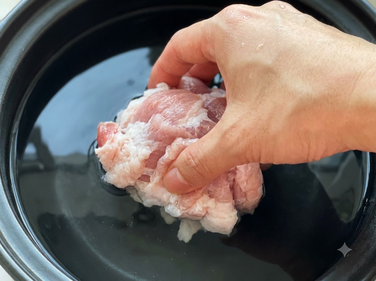Trozos de cerdo crudo sumergidos en una olla llena de agua fría y pasta de soja.