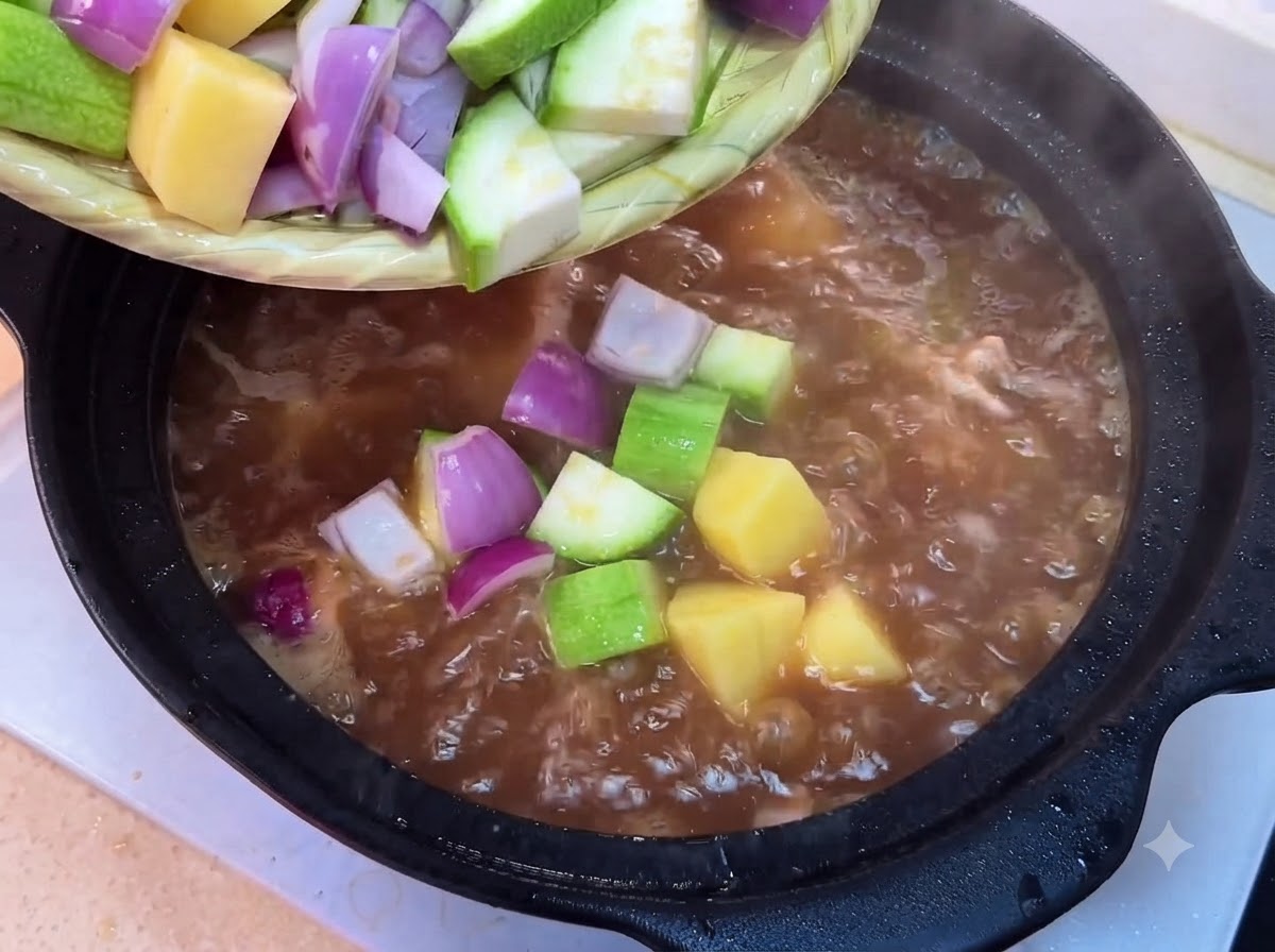 Calabacín, papas, cebollas, brotes de soja, champiñones y tofu picados siendo vertidos desde una bandeja a la olla hirviendo.