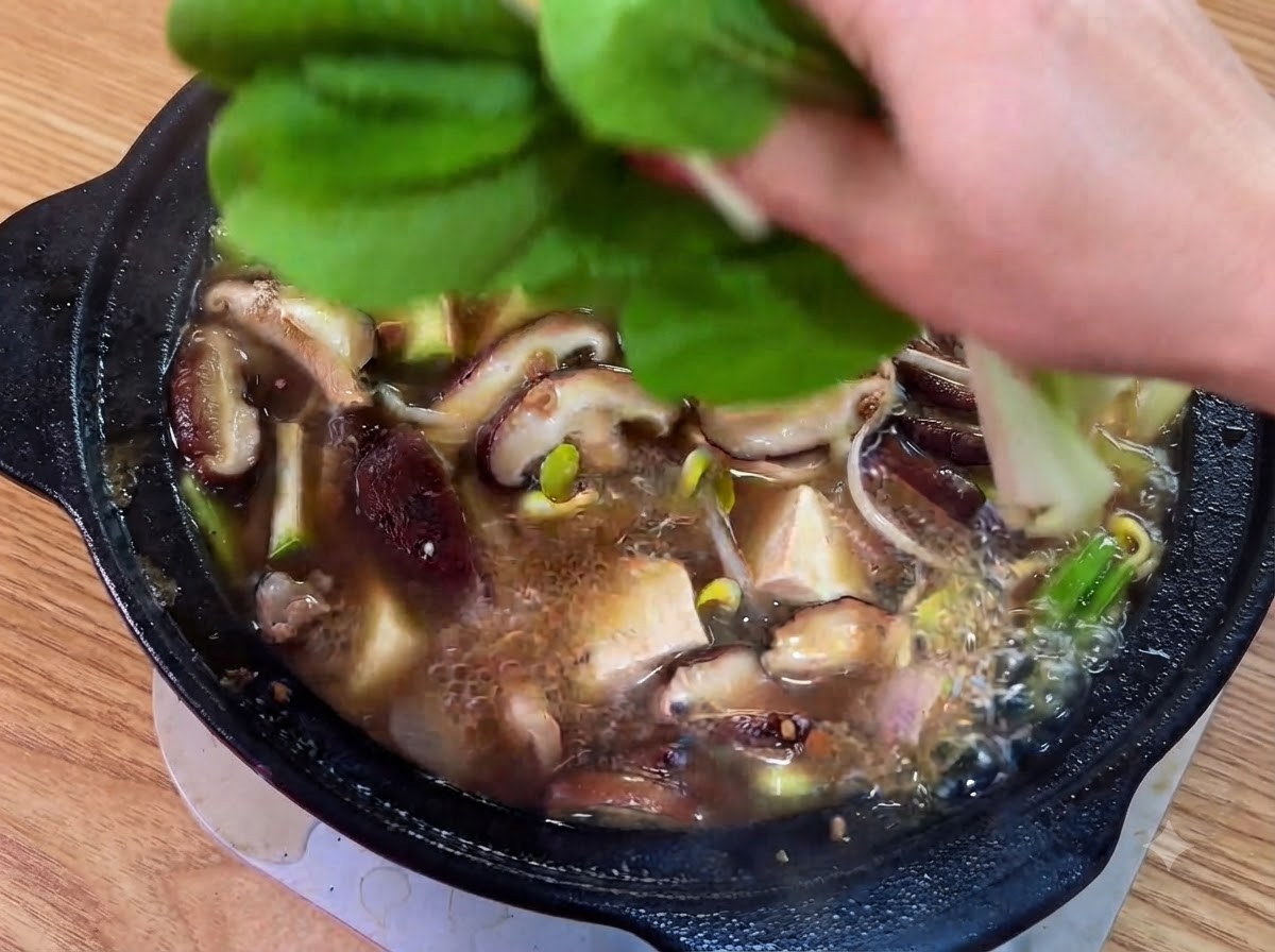 Hojas verdes frescas y chiles verdes rebanados colocados sobre el estofado cocinándose.