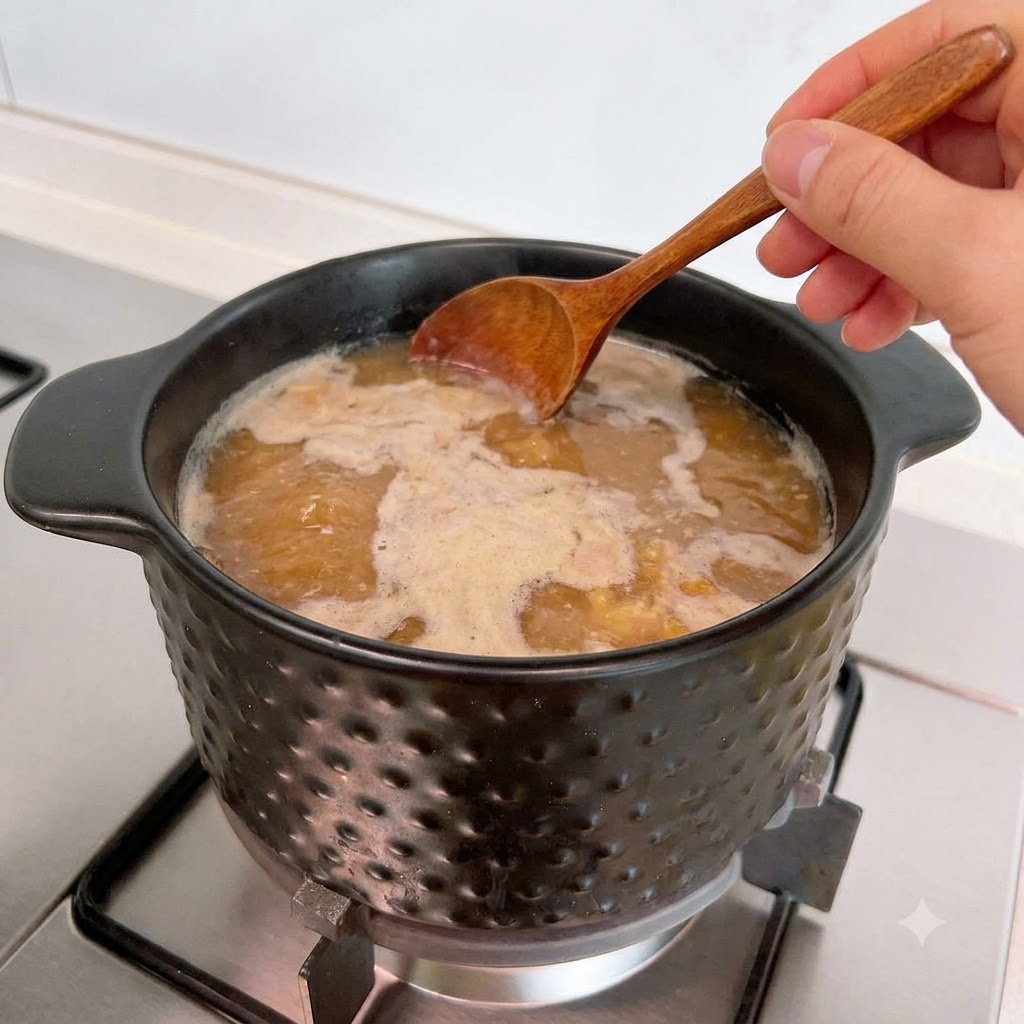 Una cuchara de madera retirando espuma de la superficie de la sopa hirviendo a fuego lento en una olla.